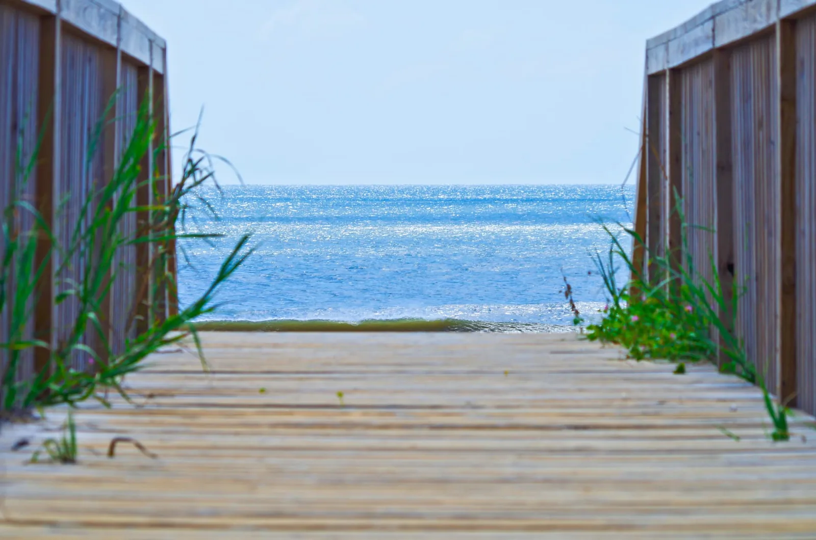 Wooden beach access walkway between two fences leading to the blue ocean at Ocean Isle Beach